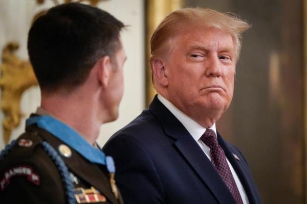 Donald Trump, wearing a blue dress suit, looks at a person in a green military jacket 